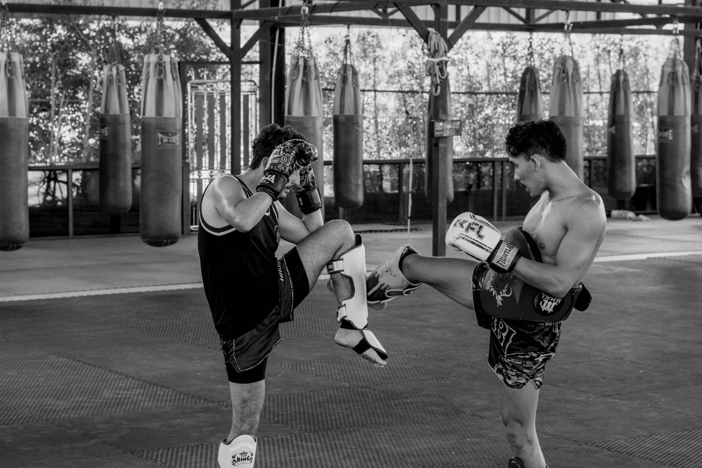 Two fighters drilling kicks in an open-air gym lined with heavy bags.